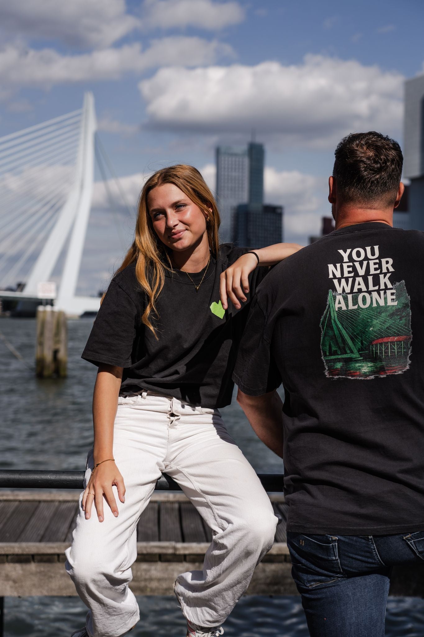 Oversized T-shirt met opdruk “YOU NEVER WALK ALONE” en illustratie van De Kuip, Erasmusbrug en skyline van Rotterdam in groen-rood kleurenpalet.