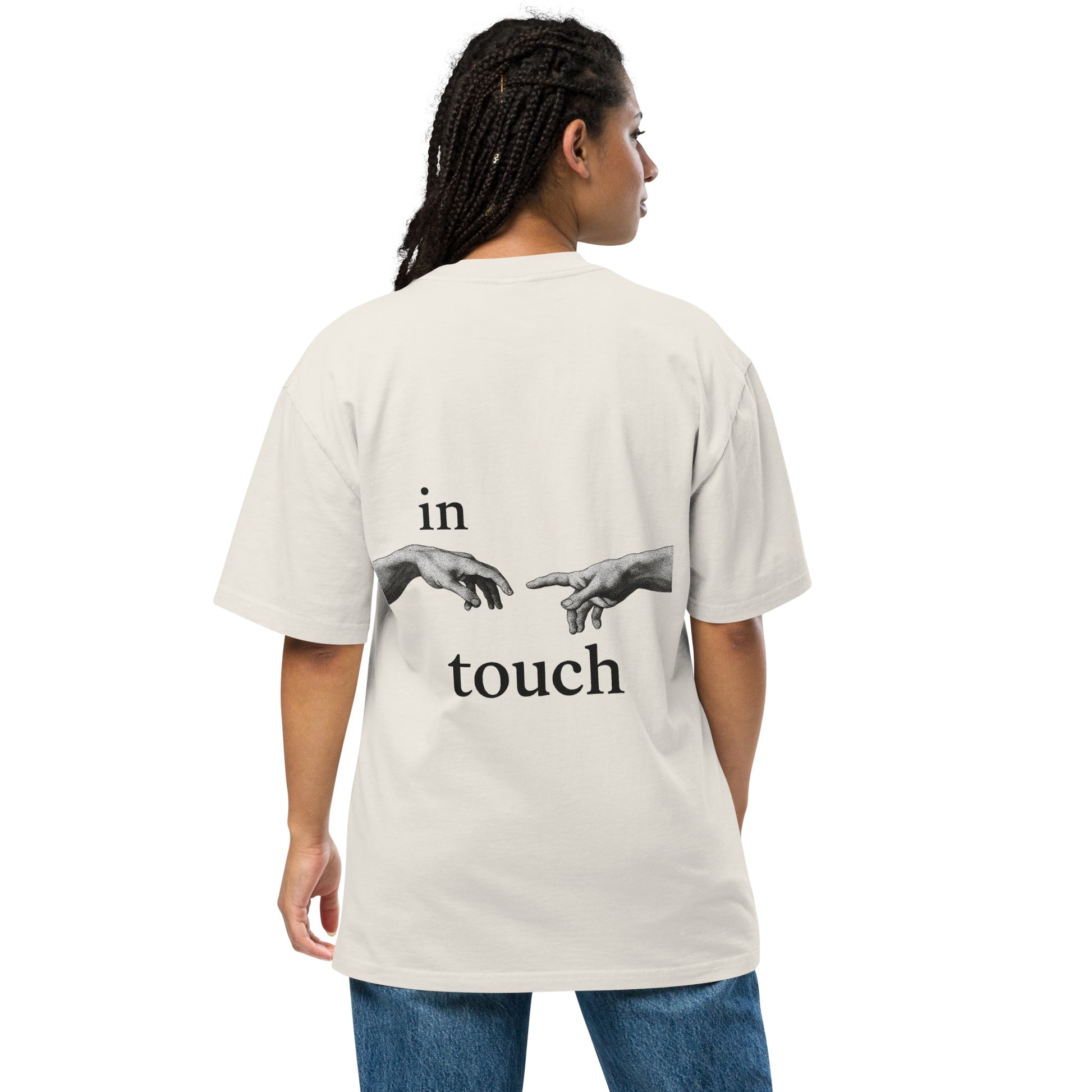 oversized T-shirt met minimalistische print van twee handen die elkaar bijna aanraken, geïnspireerd op Michelangelo’s ‘Schepping van Adam’. Gedragen door een model in urban setting.