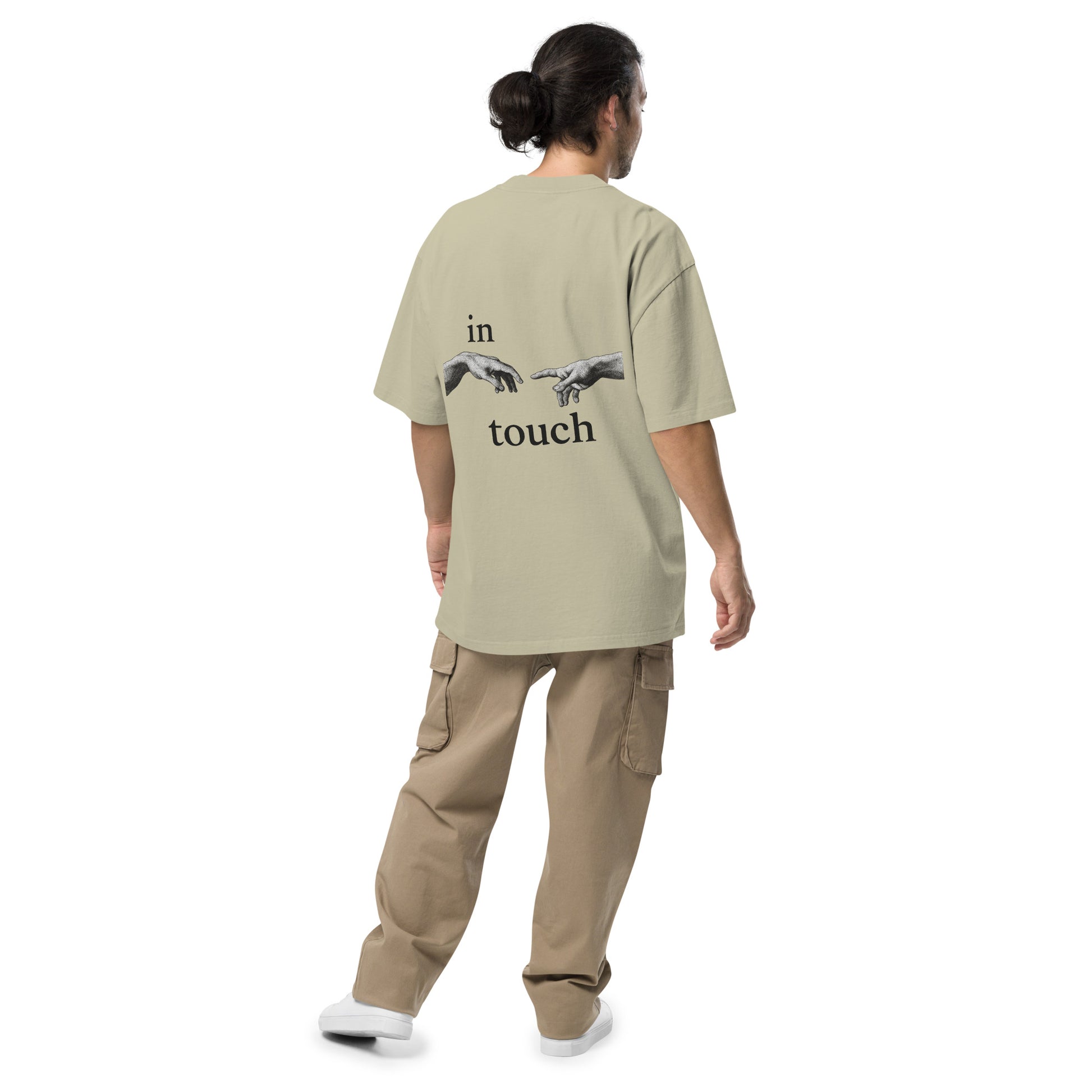 oversized T-shirt met minimalistische print van twee handen die elkaar bijna aanraken, geïnspireerd op Michelangelo’s ‘Schepping van Adam’. Gedragen door een model in urban setting.