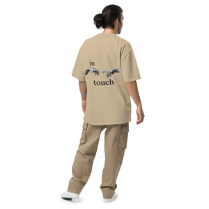 oversized T-shirt met minimalistische print van twee handen die elkaar bijna aanraken, geïnspireerd op Michelangelo’s ‘Schepping van Adam’. Gedragen door een model in urban setting.