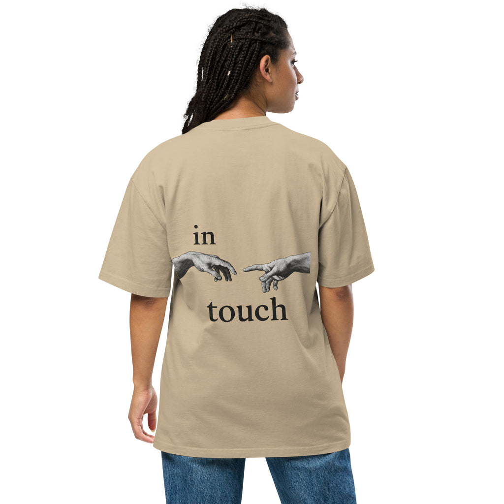 oversized T-shirt met minimalistische print van twee handen die elkaar bijna aanraken, geïnspireerd op Michelangelo’s ‘Schepping van Adam’. Gedragen door een model in urban setting.
