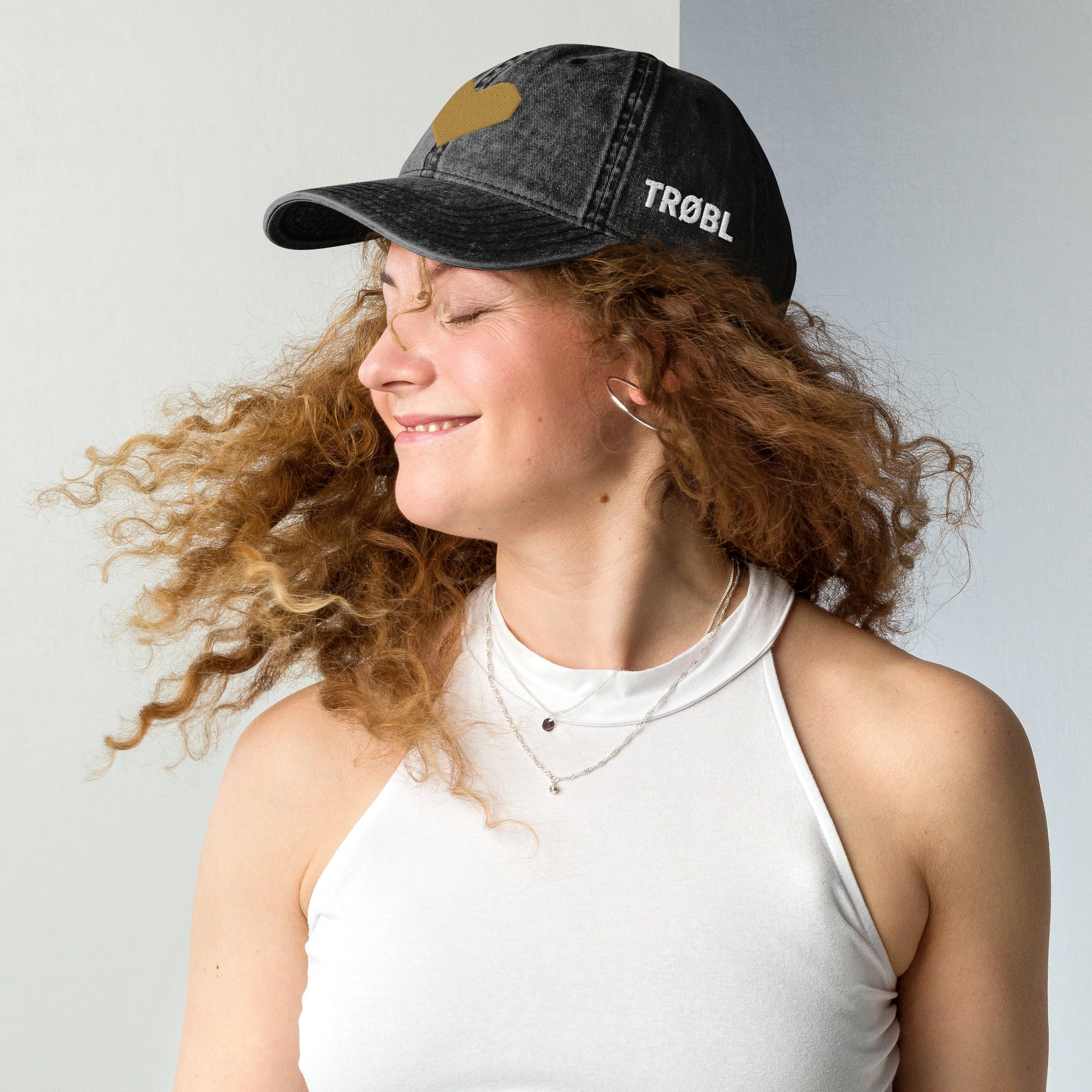TRØBL cap/pet van vintage gewassen katoen met geborduurd hart aan de voorkant en TRØBL-gouden logo aan de zijkant – unisex streetwear accessoire met ingetogen kracht.