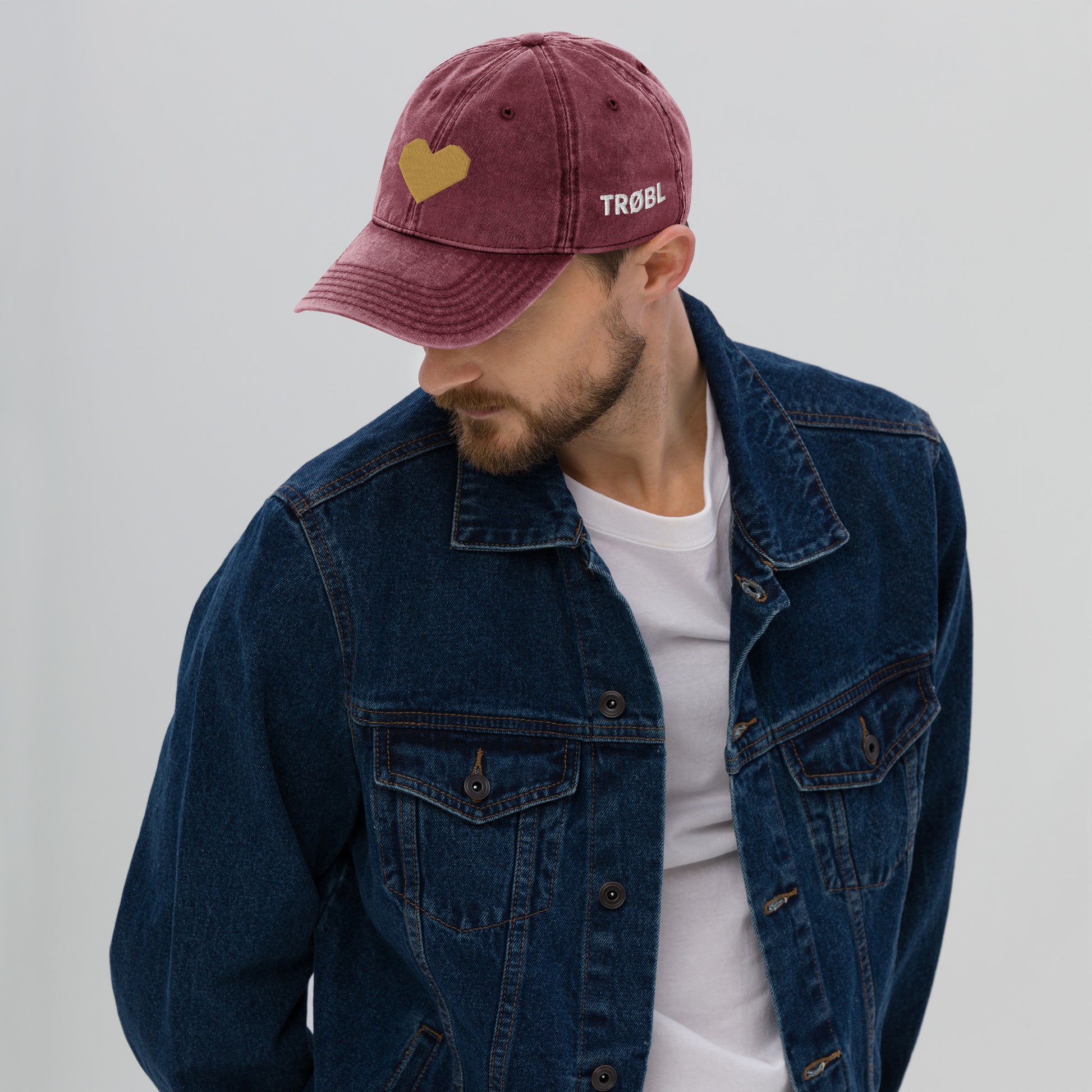 TRØBL cap/pet van vintage gewassen katoen met geborduurd hart aan de voorkant en TRØBL-gouden logo aan de zijkant – unisex streetwear accessoire met ingetogen kracht.