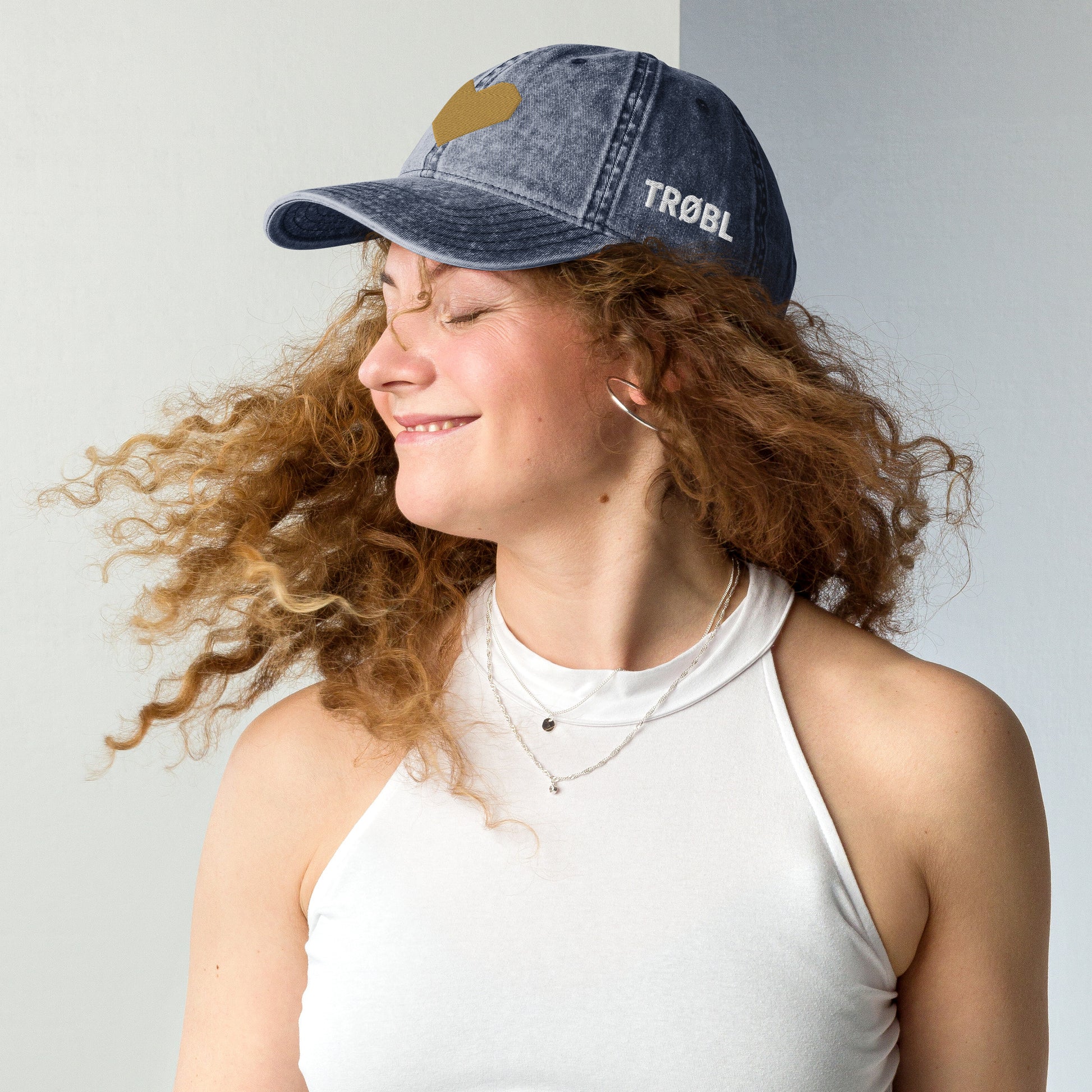 TRØBL cap/pet van vintage gewassen katoen met geborduurd hart aan de voorkant en TRØBL-gouden logo aan de zijkant – unisex streetwear accessoire met ingetogen kracht.